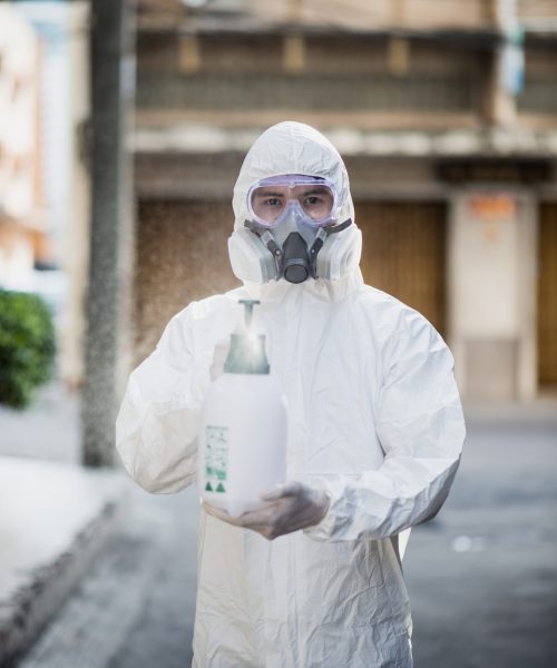 Disinfection specialist in PPE suit performing spray public deco Disinfection specialist man in personal protective equipment (ppe) suit, gloves, mask and face shield, cleaning Quarantine area with a bottle of pressurized spray disinfectant to remove coronavirus.
